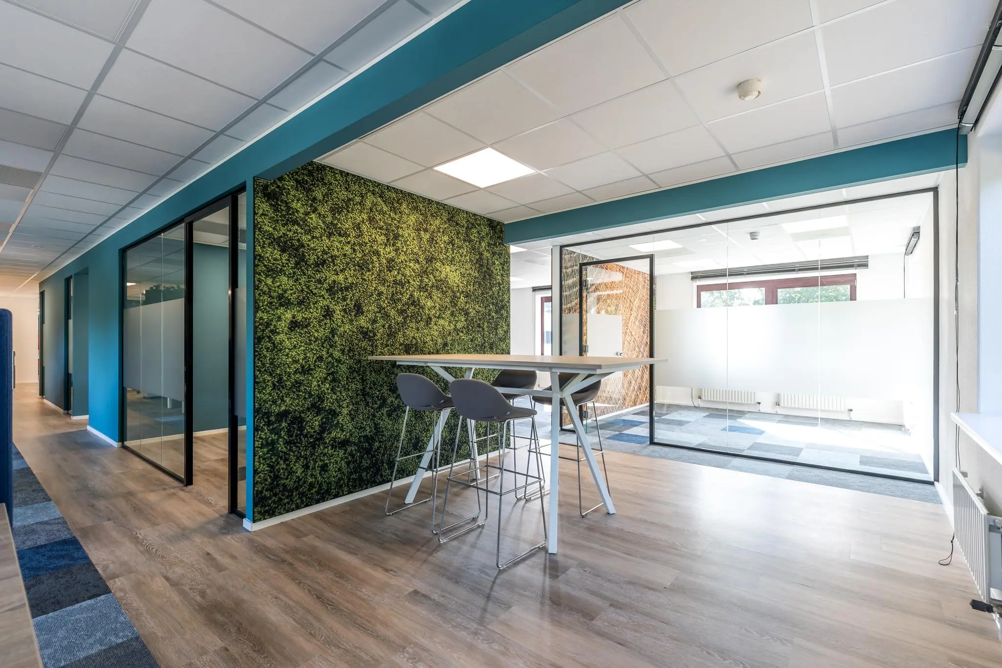 Moderne kantoorruimte aan de Baarnsche Dijk met glazen vergaderruimtes, een moswand en hoge zitplaatsen.